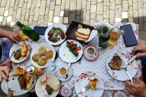 Stół zastawiony pysznym jedzeniem, typowym dla Albanii. Widać dania mięsne, gołąbki, pieczywo, kawę i piwo.