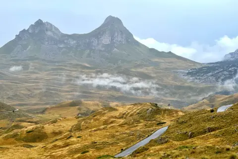 Górzyste krajobrazy Durmitor National Park, z krętymi drogami i mgłą unoszącą się nad złotymi wzgórzami.