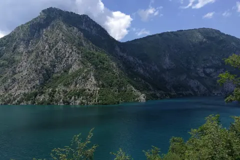 Piękne, turkusowe Pivsko Jezero otoczone skalistymi górami porośniętymi zielenią.