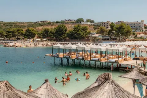 Słoneczne **ksamil dzikie plaże** z turkusową wodą, drewnianymi pomostami z leżakami i mnóstwem wypoczywających ludzi.