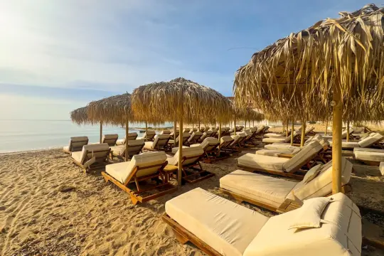 Puste leżaki pod słomianymi parasolami na piaszczystej plaży w Atenach. Spokojne morze i błękitne niebo zapraszają do relaksu.