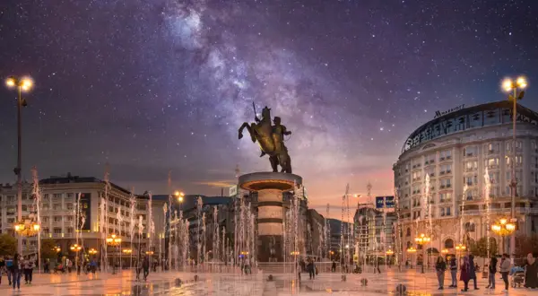 Skopje atrakcje nocą: pomnik Wojownika na koniu, fontanny i Droga Mleczna nad miastem.
