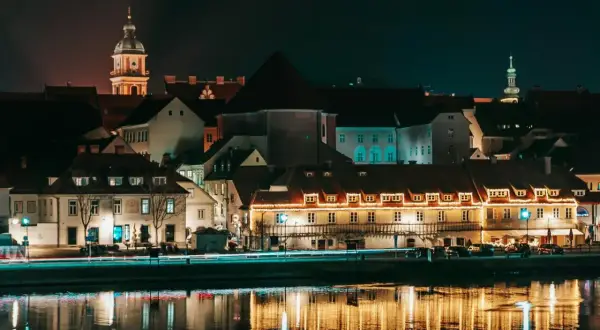 Nocny widok na zabytkowe budynki w Mariborze, Słowenia, z odbiciami świateł w rzece.