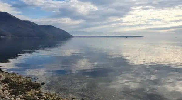 Spokojne morze w Czarnogórze we wrześniu. Góry w oddali, chmury odbijające się w wodzie.