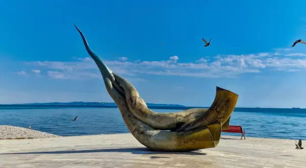 Monumentalna rzeźba na promenadzie w Durrës, plaża w tle, błękitne niebo i morze.
