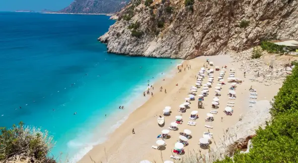 Malownicza plaża w Turcji z turkusową wodą i skalistymi klifami. Rzędy leżaków i parasoli zapraszają do odpoczynku.