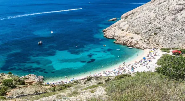 Rajska plaża w Baška Chorwacja, z turkusową wodą, łodziami i mnóstwem plażowiczów.