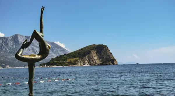 Posąg tancerki na tle gór i morza, idealne miejsce na balkan trip.