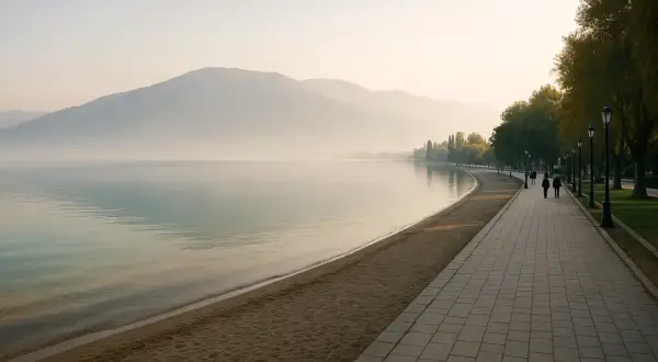 Spokojny poranek nad jeziorem w Pogradec, Albania. Mgła otula góry, a spacerowicze cieszą się spokojem promenady.