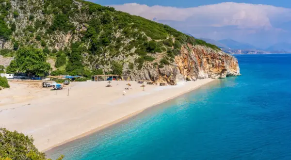 Piękna plaża Dhermi z turkusową wodą, skalistym klifem i zielonymi wzgórzami.