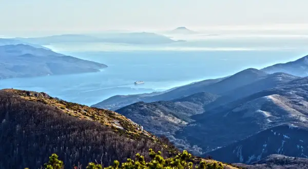 Widok z Učka Nature Park na zatokę z kontenerowcem. Góry w odcieniach niebieskiego i zieleni.