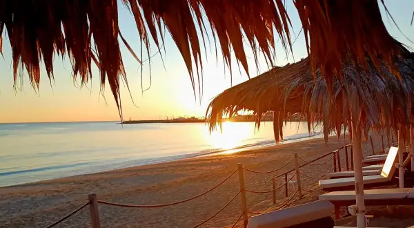 Zachód słońca na plaży w Ayia Napa. Leżaki pod słomianymi parasolami czekają na turystów. Idealne miejsce, by zobaczyć piękno Cypru.