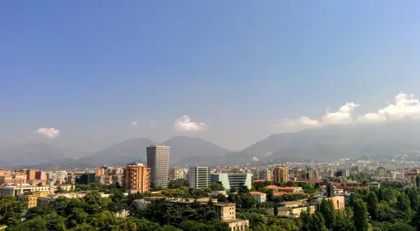 Widok na miasto z górami w tle. Widać nowoczesne budynki i zieleń. Idealne miejsce na **Albania roaming** i odkrywanie krajobrazów.