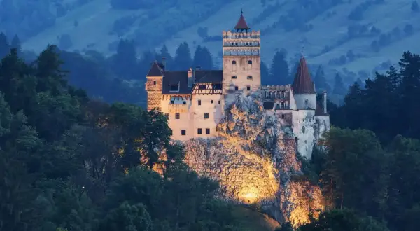 Zamek Bran w Transylwanii, oświetlony nocą, na tle zalesionych wzgórz.