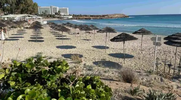 Puste cypr plaże z rzędami parasoli i hotel w tle. Słońce rzuca długie cienie na piasek.