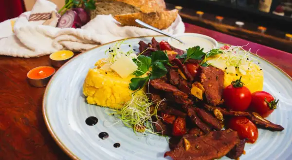 Pyszne jedzenie w Rumunii: polenta z wołowiną, pomidorkami i serem. Obok świeży chleb i świece tworzą przytulną atmosferę.