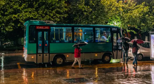 Deszczowa noc w Tiranie. Ludzie z parasolami czekają na autobus do Durrës.