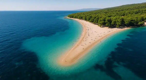 Widok z lotu ptaka na piaszczysty cypel otoczony turkusową wodą. Rajskie plaże z zielonym lasem w tle.