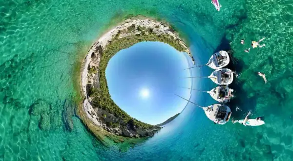 Rajskie **peloponez plaże** z krystalicznie czystą wodą, żaglówkami i ludźmi kąpiącymi się w słońcu.