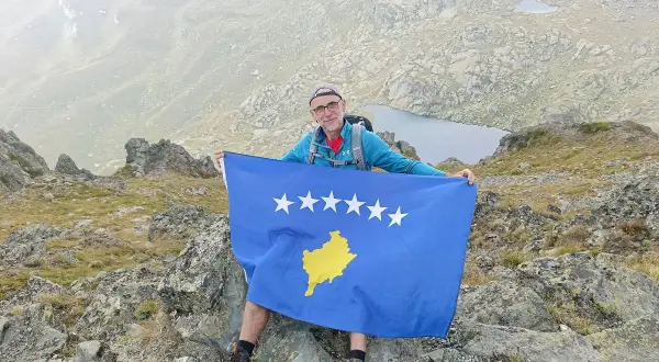 Mężczyzna z flagą Kosowa na szczycie góry. Niesamowite kosowo wakacje w górach.