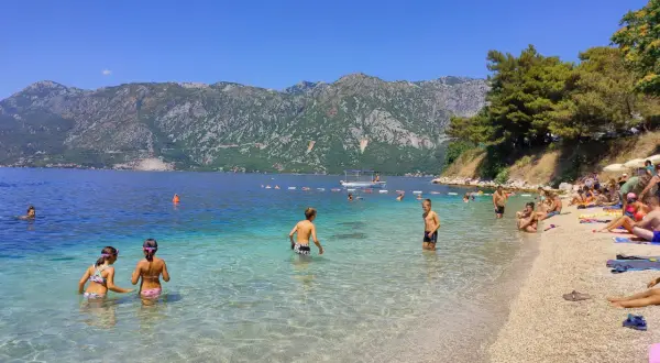 Słoneczny dzień na Perast beach. Ludzie kąpią się w krystalicznie czystej wodzie, podczas gdy góry w tle tworzą malowniczy krajobraz.
