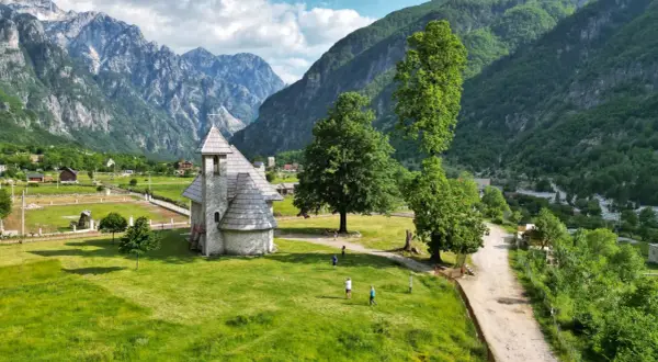 Kamienna cerkiew w Theth, Albania, otoczona zielonymi wzgórzami i majestatycznymi górami.