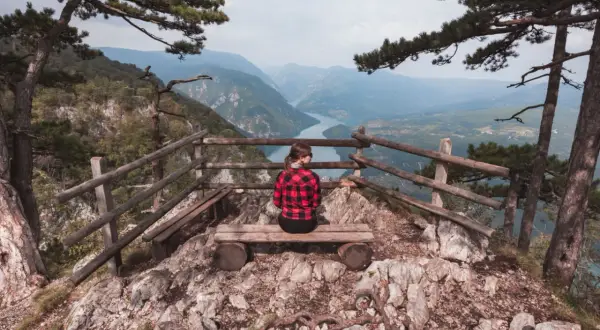 Widok na rzekę z punktu widokowego w Serbii. Kobieta w kratę siedzi na ławce, podziwiając krajobraz. Serbia atrakcje.