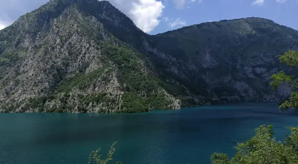 Piękne, turkusowe Pivsko Jezero otoczone skalistymi górami porośniętymi zielenią.