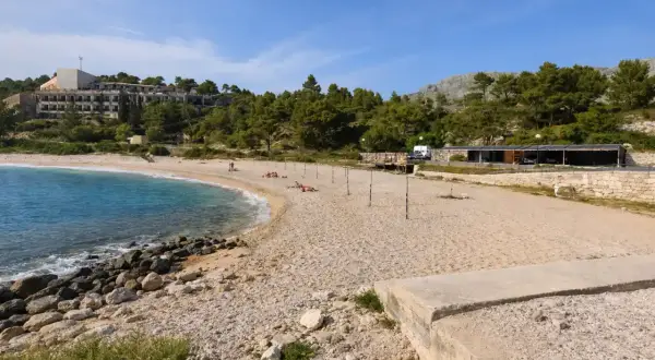 Plaża w Kupari, Chorwacja, z turkusową wodą, kamienistym brzegiem i hotelami w tle.