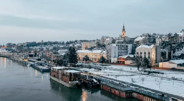 Zimowy Belgrad nad Dunajem, z ośnieżonymi budynkami i statkami. Czy Serbia jest bezpieczna? Widok sugeruje spokojne miasto.