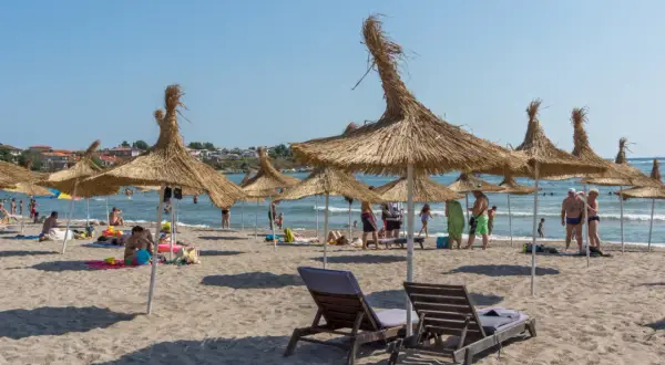Słoneczna plaża z parasolami z trawy, leżakami i ludźmi cieszącymi się wakacjami. To idealne miejsce na **carewo atrakcje**.