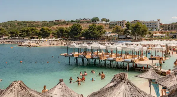 Słoneczne **ksamil dzikie plaże** z turkusową wodą, drewnianymi pomostami z leżakami i mnóstwem wypoczywających ludzi.