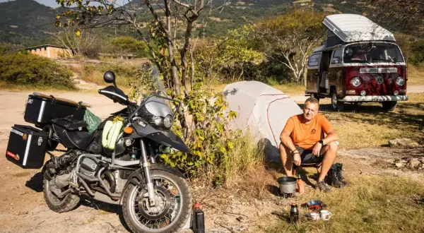 Motocykl, namiot i kamper to idealny zestaw, by wiedzieć, co zabrać na camping. Mężczyzna gotuje na kuchence turystycznej.