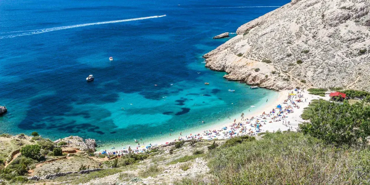 Rajska plaża w Baška Chorwacja, z turkusową wodą, łodziami i mnóstwem plażowiczów.