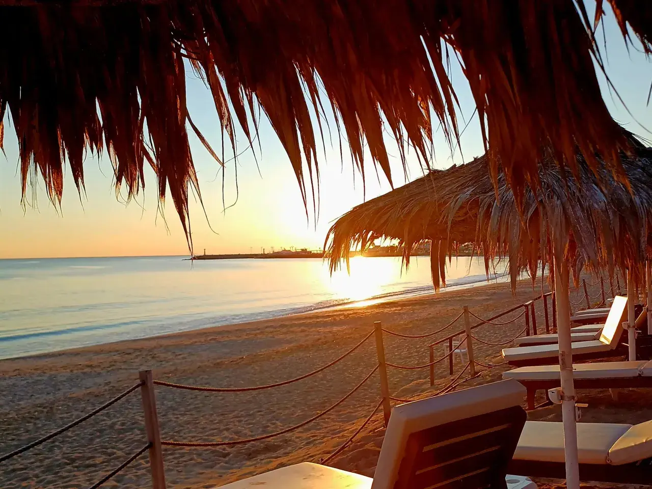 Zachód słońca na plaży w Ayia Napa. Leżaki pod słomianymi parasolami czekają na turystów. Idealne miejsce, by zobaczyć piękno Cypru.