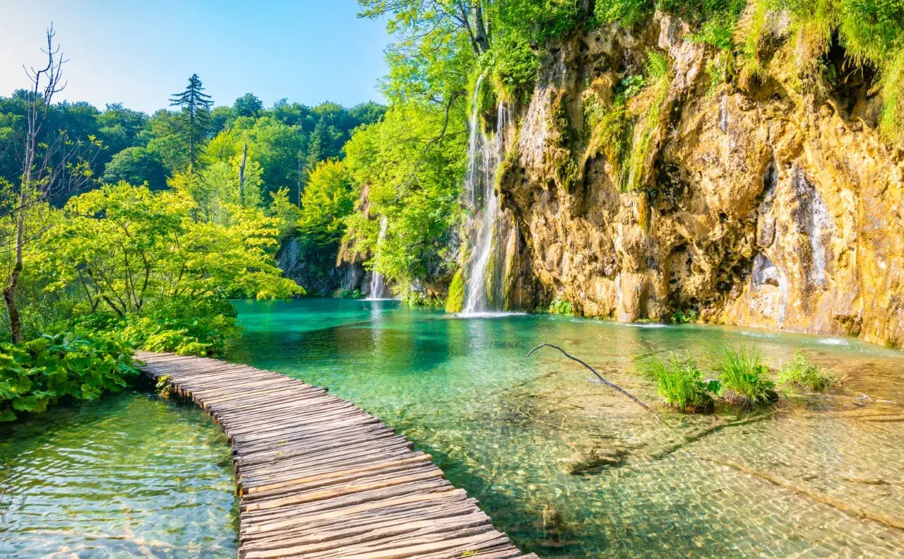 Malownicze chorwackie wodospady w Plitwicach, z drewnianą kładką wijącą się nad turkusową wodą.
