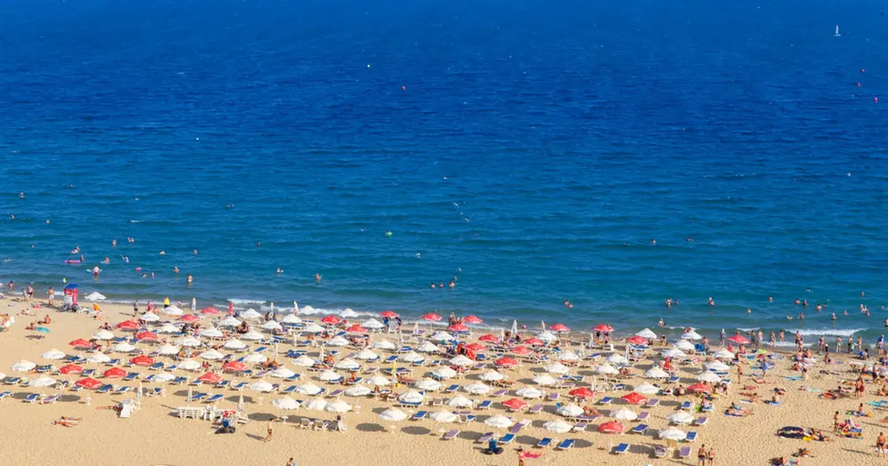 Słoneczny brzeg tętni życiem. Tłumy plażowiczów odpoczywają pod parasolami, kąpią się w morzu i opalają na piasku.