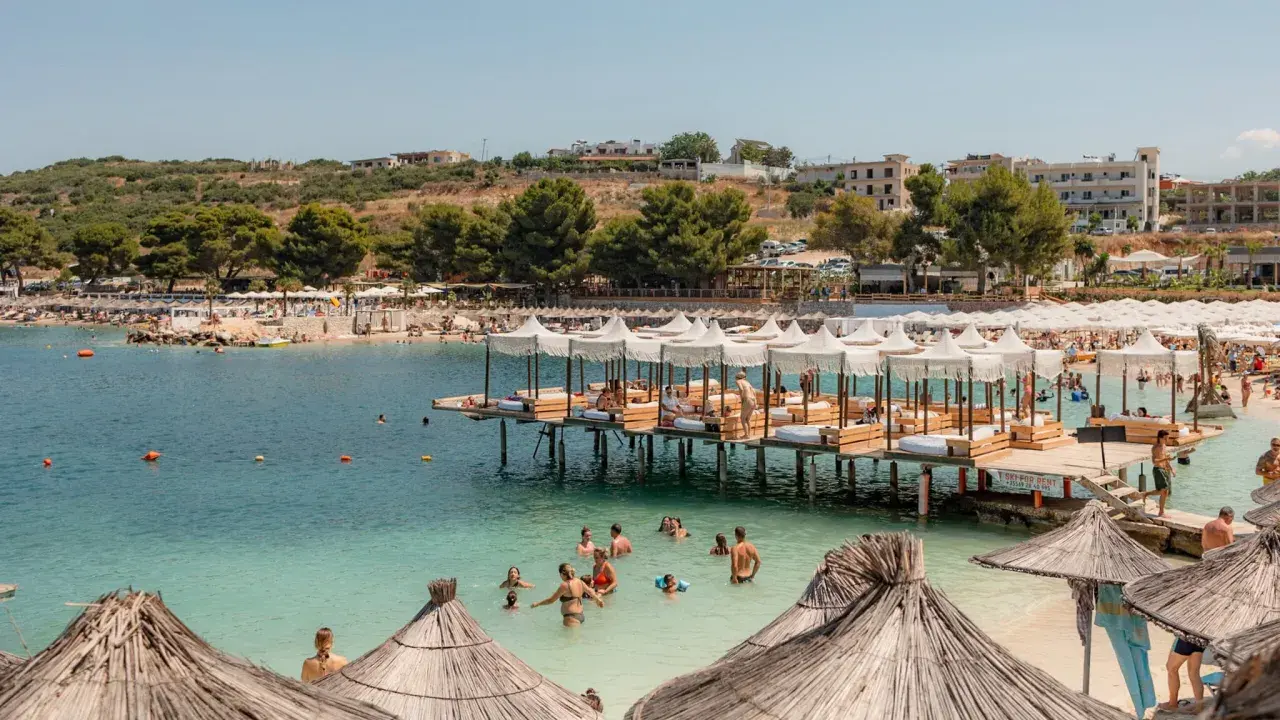 Słoneczne **ksamil dzikie plaże** z turkusową wodą, drewnianymi pomostami z leżakami i mnóstwem wypoczywających ludzi.