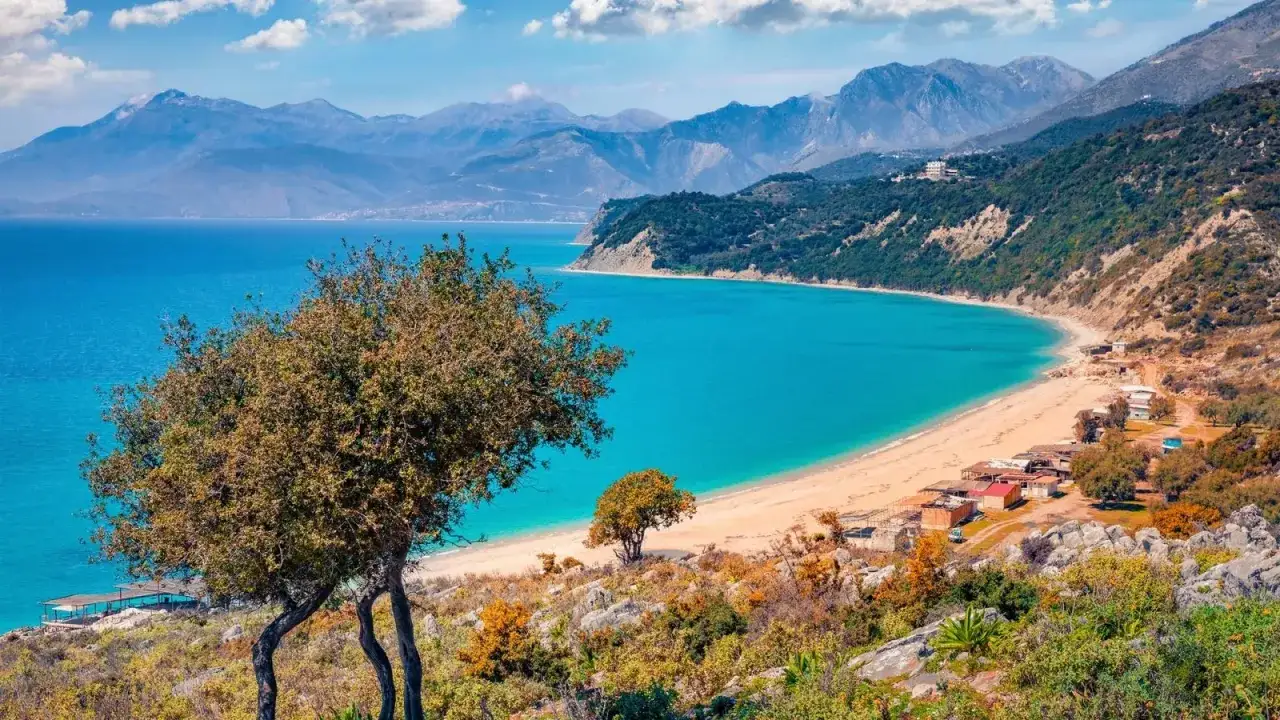 Albania gdzie na wakacje? Piękna, piaszczysta plaża z turkusową wodą, otoczona górami i zielenią. Idealne miejsce na relaks.