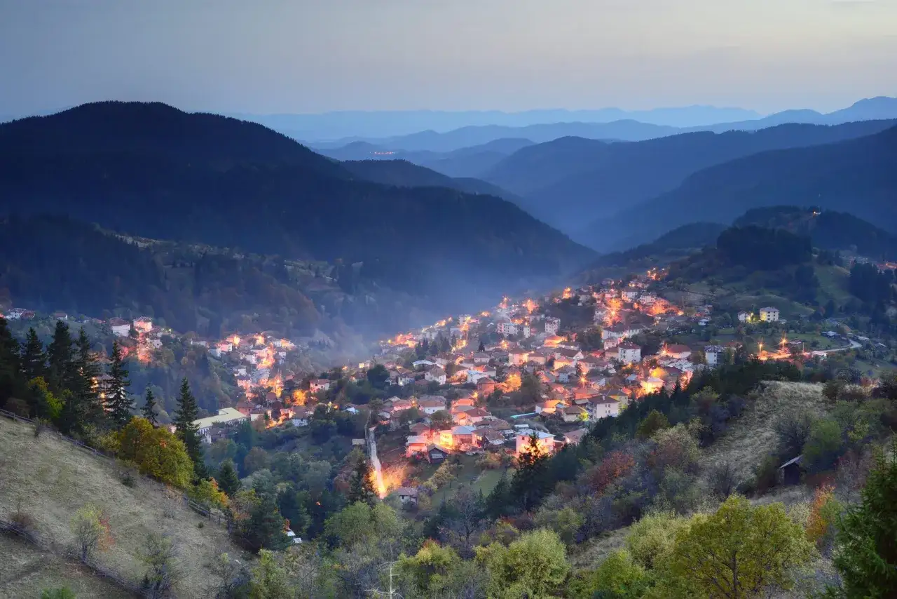 Wieczorna panorama gór Pirin z oświetloną wioską w dolinie.