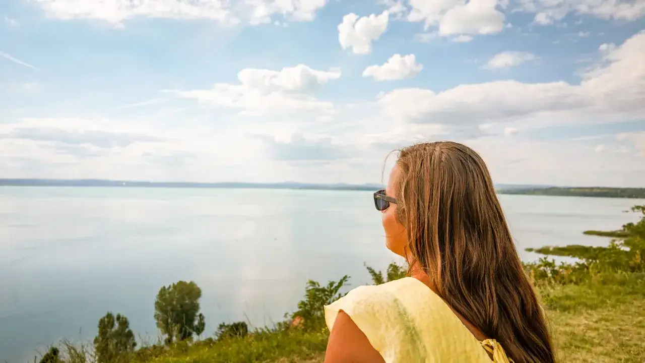 Kobieta w żółtej bluzce podziwia rozległy Balaton na Węgrzech.