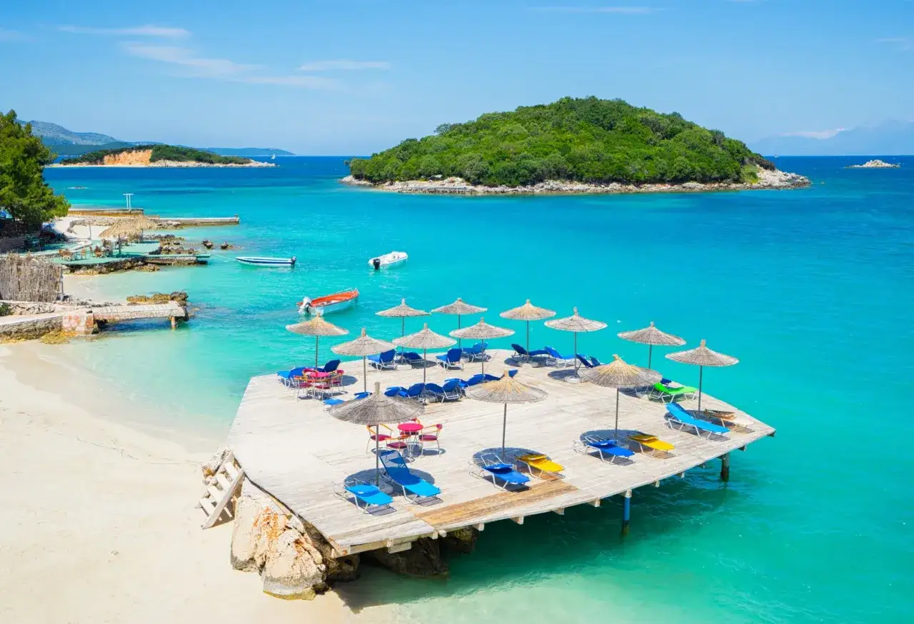 Albania, gdzie najpiękniej: turkusowe morze, piaszczysta plaża i drewniany pomost z leżakami i parasolami.