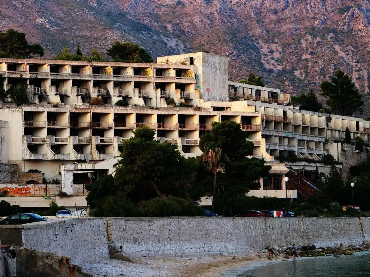 Opuszczony hotel nad morzem, zniszczone balkony i okna, góry w tle. To miejsce to prawdziwa zatoka umarłych hoteli.