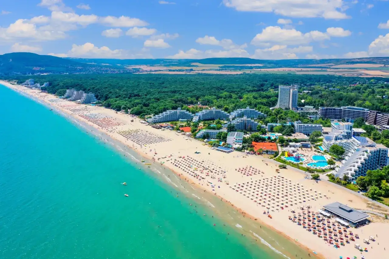 Słoneczna plaża w Bułgarii z mnóstwem leżaków i hoteli. Zastanawiasz się, ile kosztuje lot do Bułgarii?