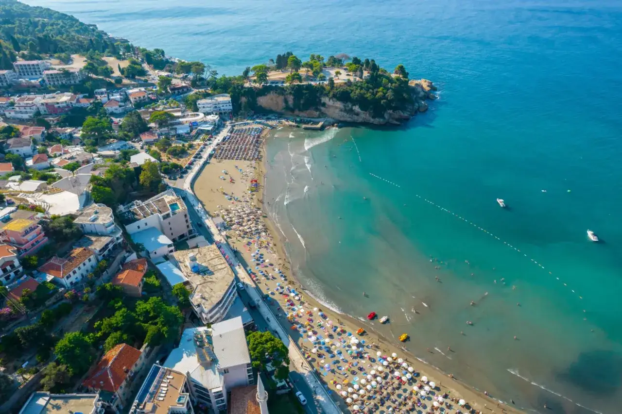 Malownicze czarnogóra widoki: zatłoczona plaża, turkusowe morze i miasteczko na wzgórzu.