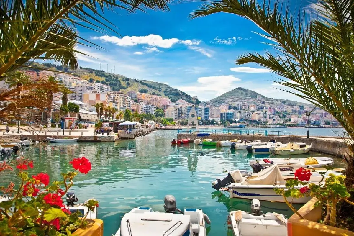 Malowniczy port z łodziami i palmami, w tle kolorowe albania miasta na wzgórzu.