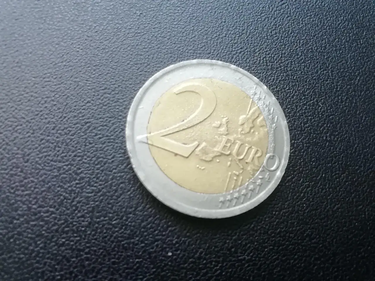 Moneta dwueuro, która jest walutą w Kosowie, leży na czarnej, teksturowanej powierzchni.
