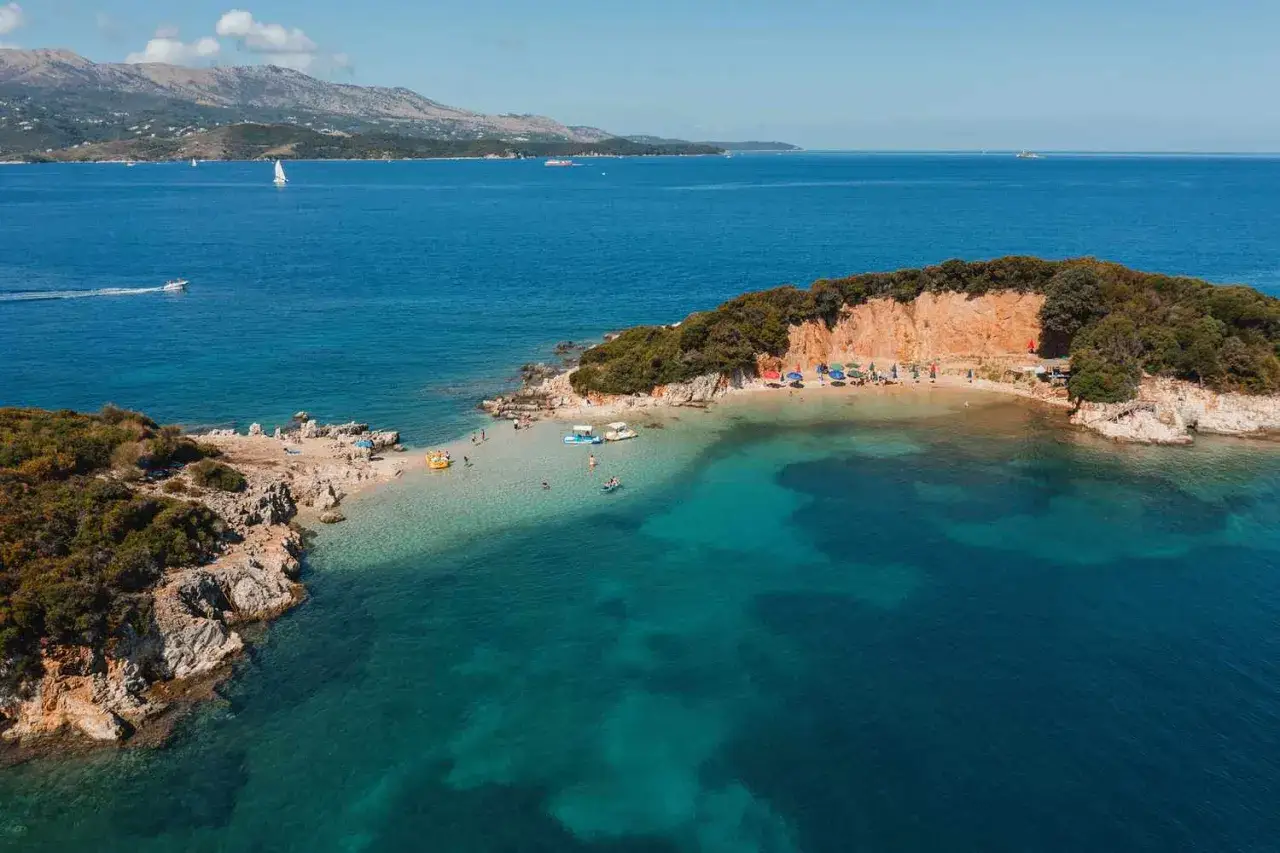 Malowniczy dhermi beach z turkusową wodą, skalistymi brzegami i zielonymi wzgórzami w tle.