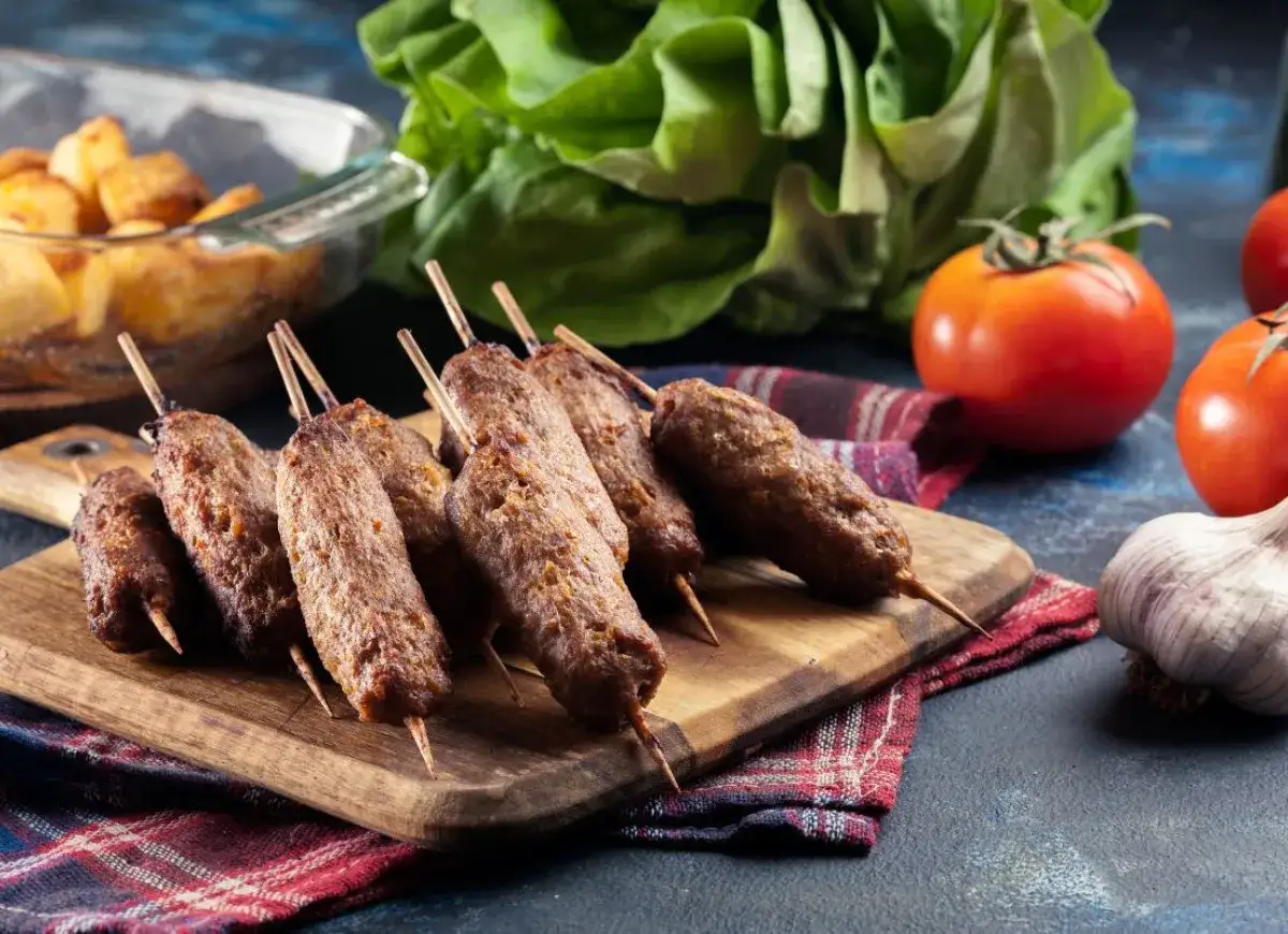 Pyszne cevapcici na patyczkach, gotowe do podania. Idealne na grilla, z dodatkiem świeżych warzyw.