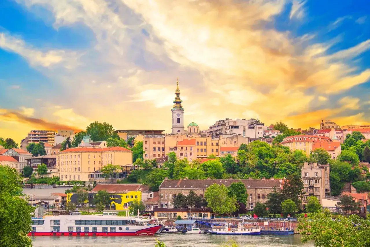 Widok na Belgrad z rzeką i statkami. Miasto z wieżą kościelną i zielenią, zachęca do podróży, odpowiadając na pytanie: czy Serbia jest bezpieczna?